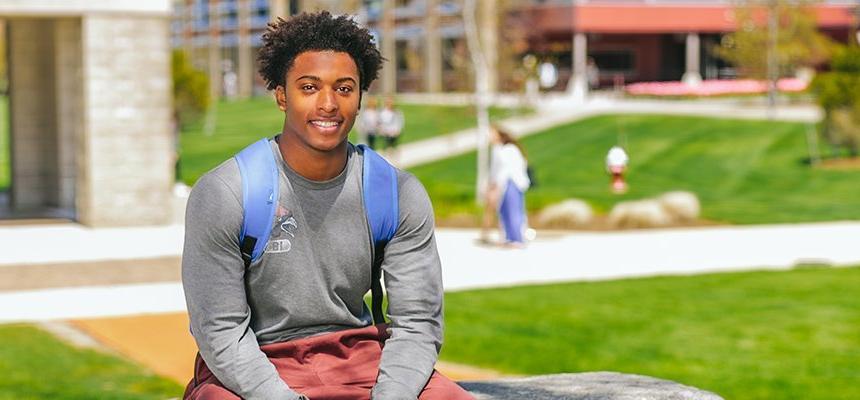 Students sits on a bench on the Bristol campus and smiles at the camera